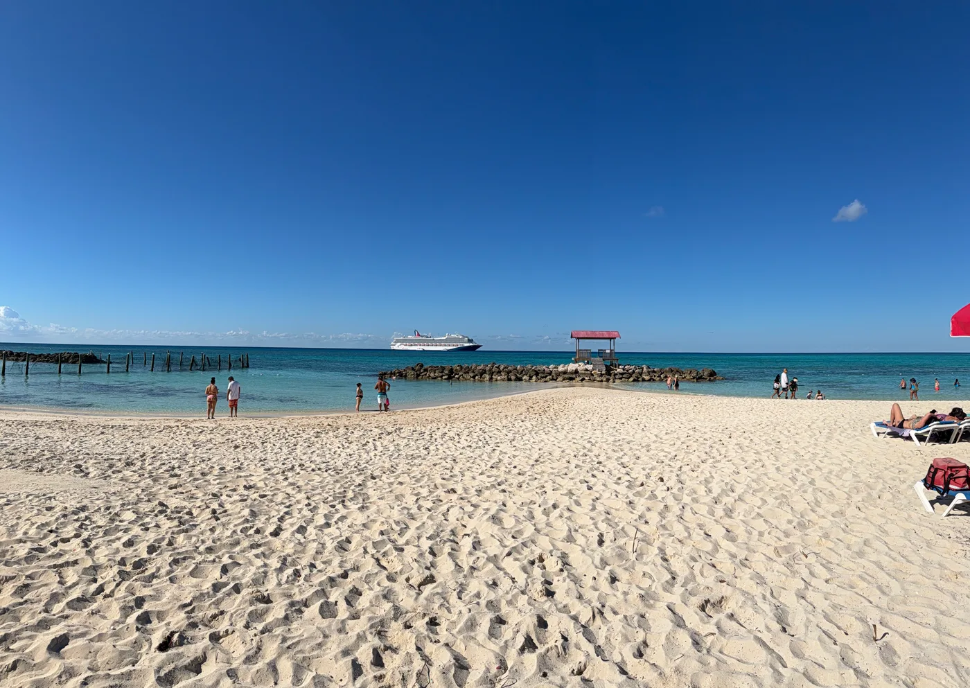 A wide white beach running out to a pier, with a ship far out on the horizon