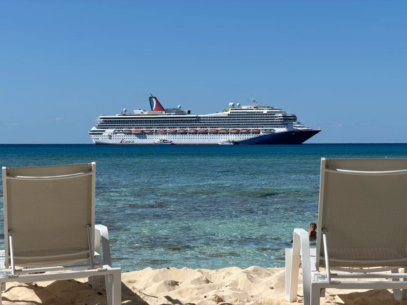 A cruise ship at anchor, seen from between two beach loungers