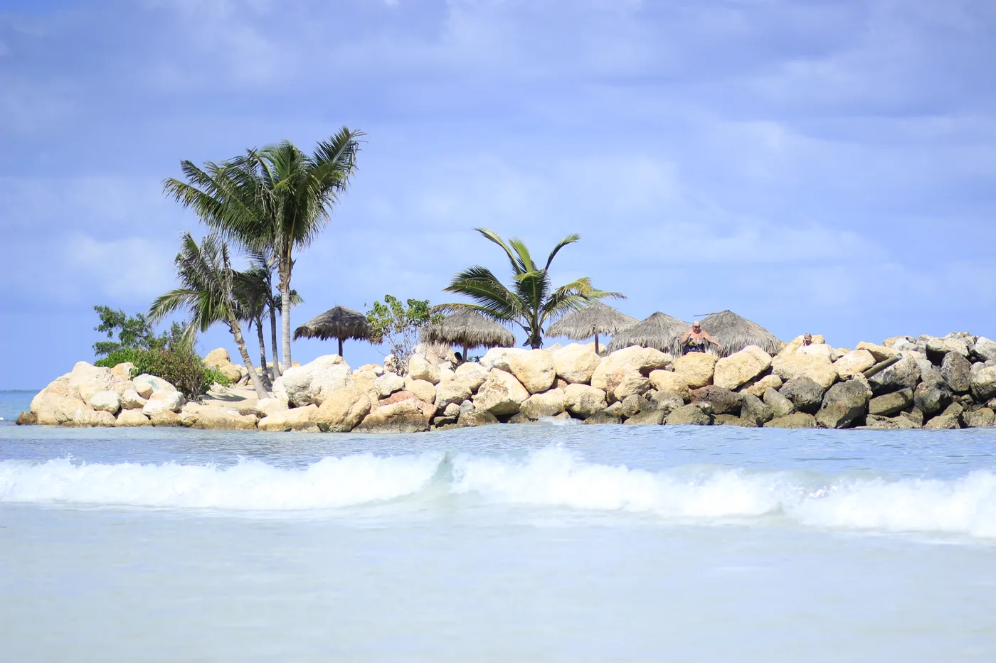 Surf rolling past a rock breakwater lined with palms