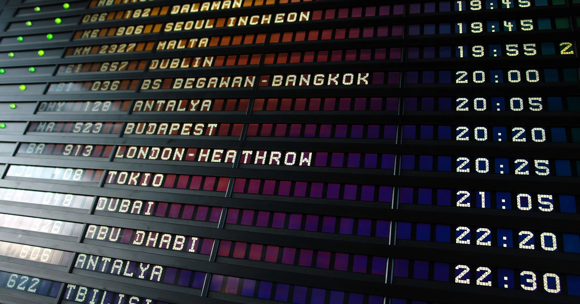 A split-flap airport departure board listing international destinations and departure times.