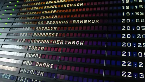 A split-flap airport departure board listing international destinations and departure times.